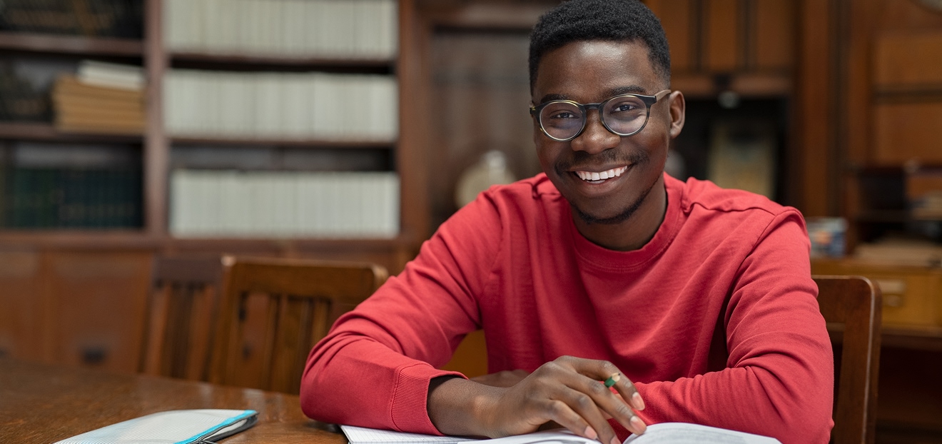 Étudiant souriant travaillant avec un livre ouvert dans une bibliothèque