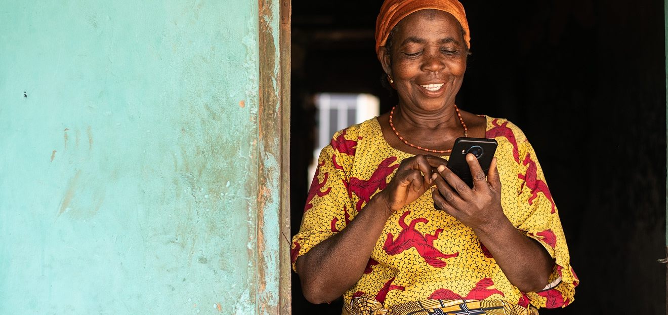 Femme âgée souriante utilisant un smartphone devant une maison colorée