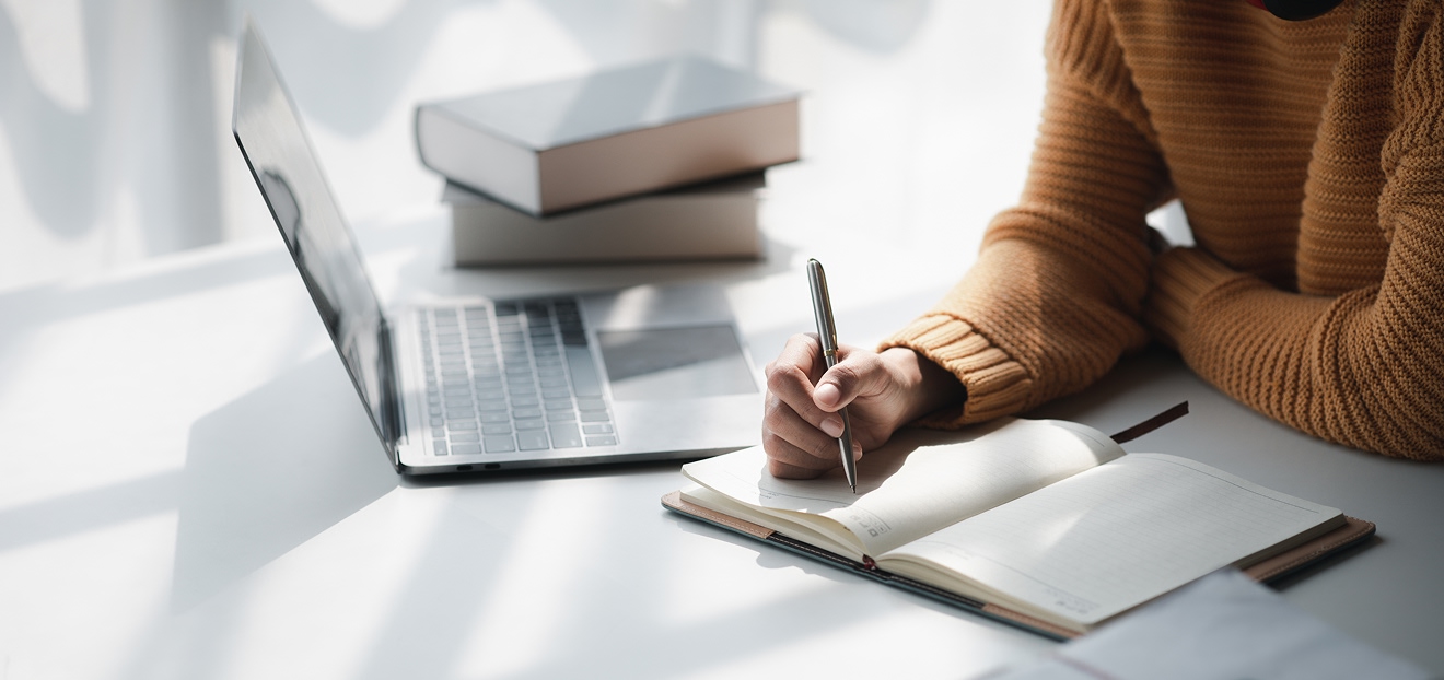 Personne prenant des notes dans un carnet avec ordinateur portable et livres de travail