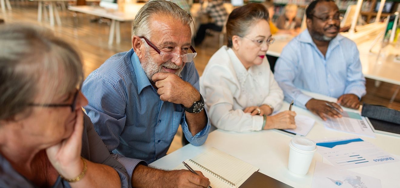 Groupe d’adultes âgés travaillant ensemble autour d’une table avec documents et notes dans une salle d’étude